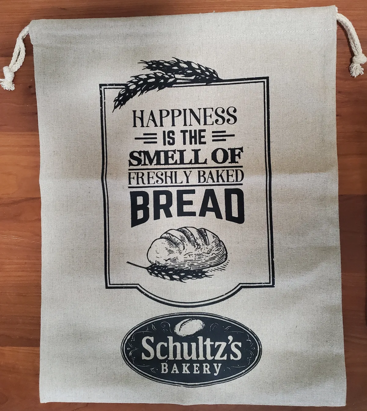 Natural linen drawstring bread bag printed with 'Happiness is the smell of freshly baked bread' and the Schultz's Bakery logo